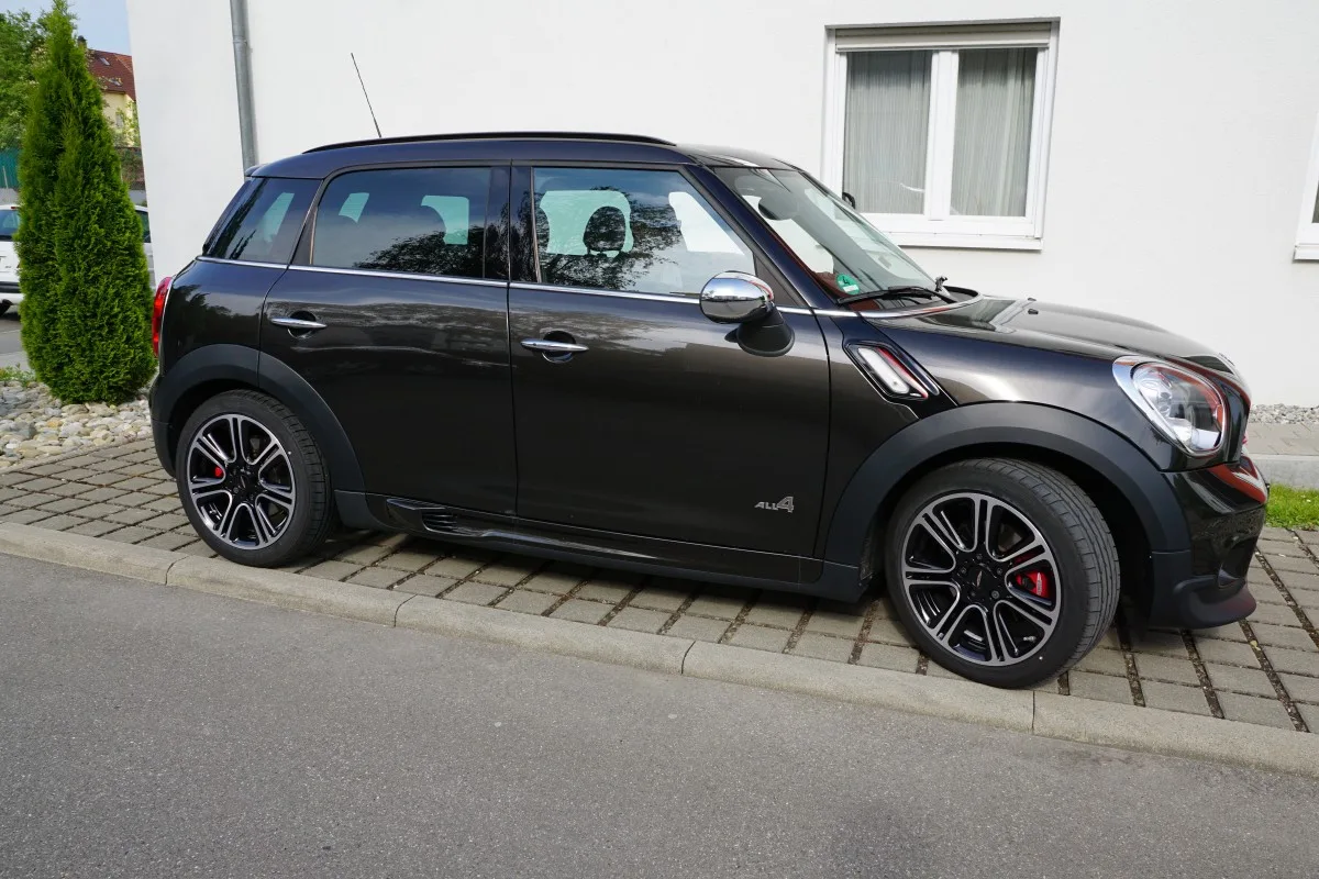 Black Mini Cooper Countryman parked on a paved surface beside a building.